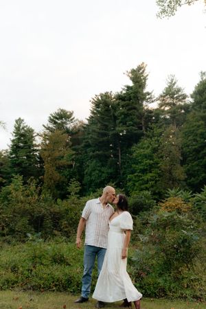 A couple embraces in a natural woodland setting surrounded by tall pine trees.