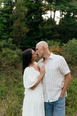 A tender moment between a couple sharing a kiss against a backdrop of pine trees.