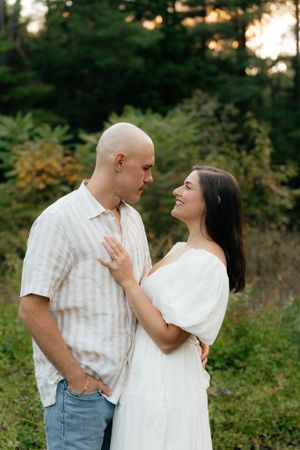 A couple shares an intimate moment while standing in a meadow surrounded by evergreens.