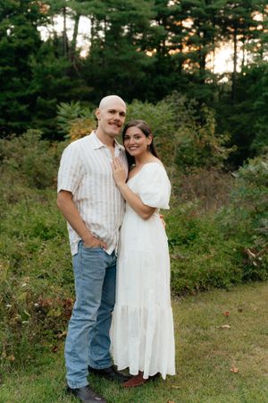 A couple poses casually together in a forest clearing at sunset wearing coordinated outfits.