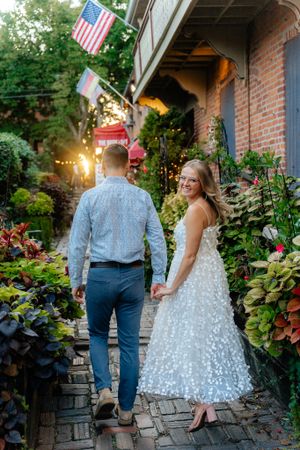 Couple walking up garden path with American flag and twinkling lights in background.