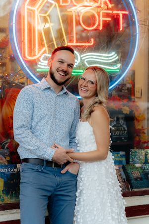 Couple poses beneath colorful neon Book Loft sign in vintage storefront.