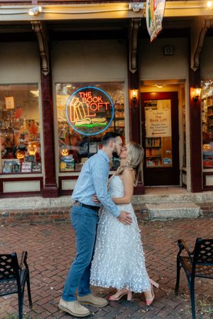 Romantic moment outside The Book Loft storefront with neon sign glowing above.