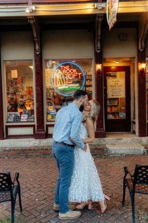 Tender moment shared outside bookstore with illuminated neon sign in background.