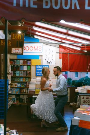 A romantic moment captured in a bookstore as a couple in formal wear dances among the bookshelves.