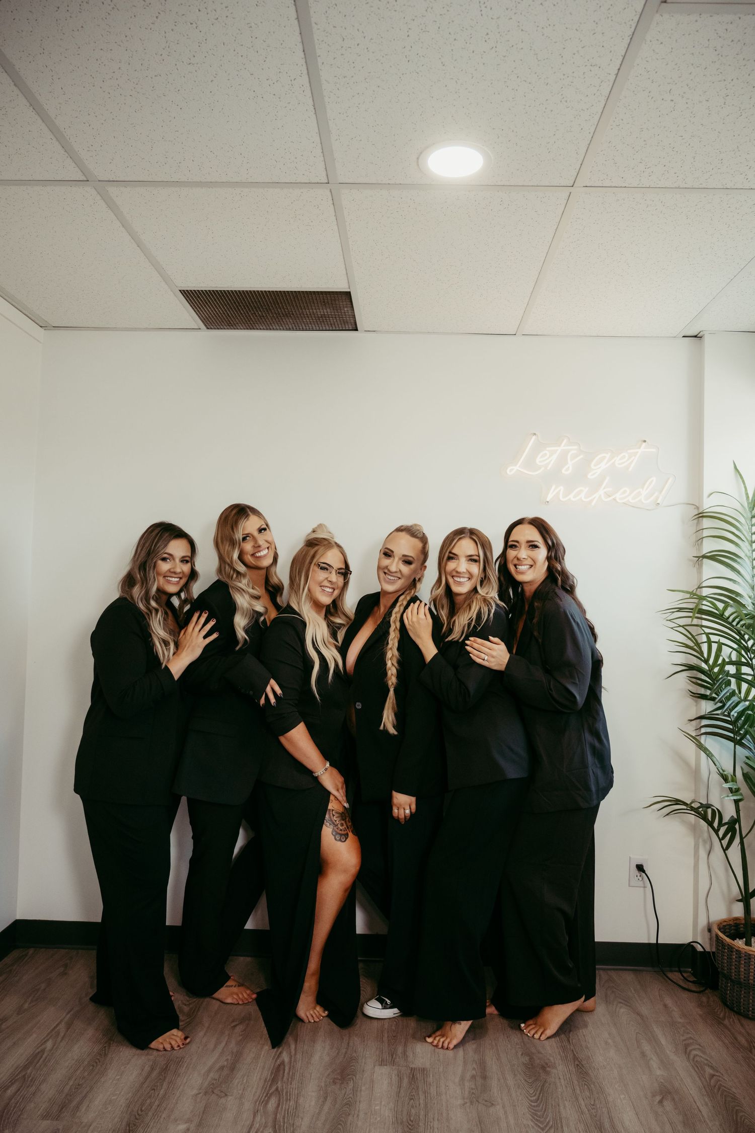 Group of women in elegant black outfits posing together for a celebratory photo indoors.