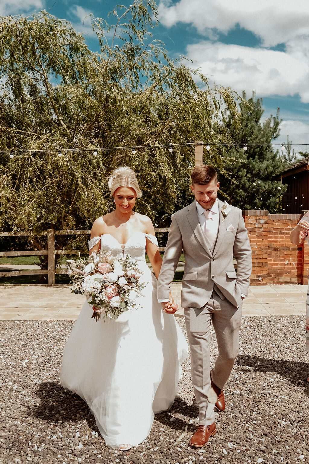 Bride and groom walking hand in hand in court yard at Coton House Farm wedding venue, the bride holding a large bouquet.