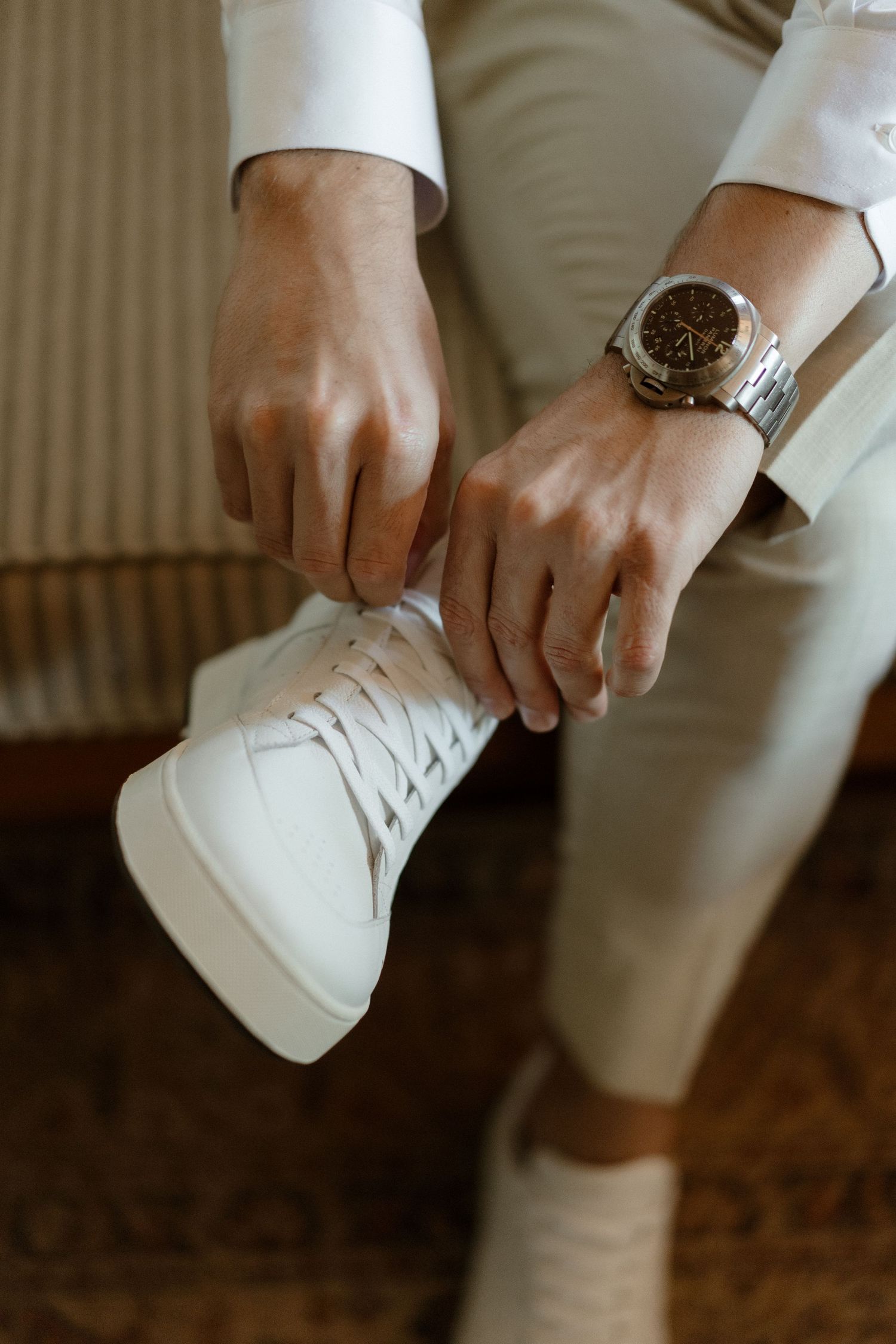 Close-up of hands adjusting white sneakers with a stylish watch visible on the wrist.