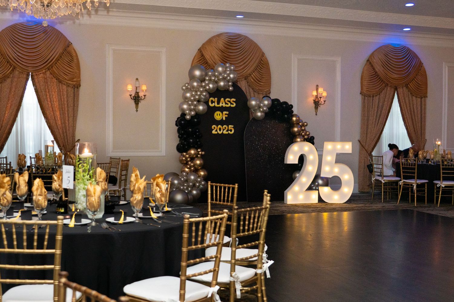 Elegant Class of 2025 graduation party venue with black and gold balloon arch and large number decor.