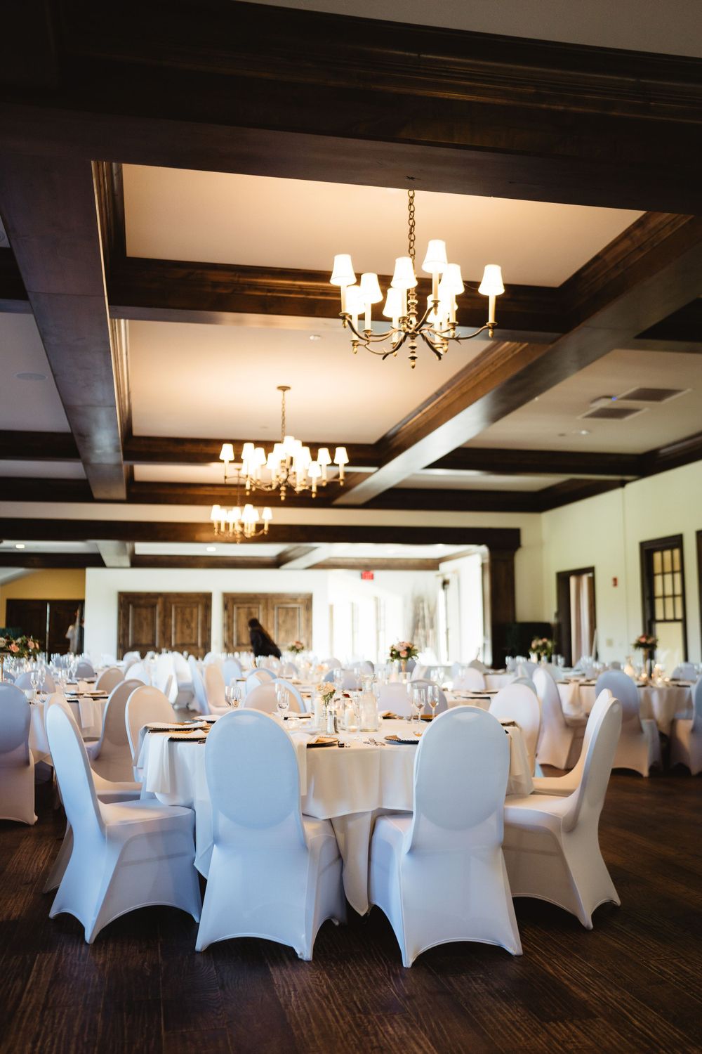 Elegant wedding reception hall with exposed wooden beams and white spandex chair covers.