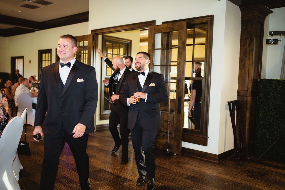 Groomsmen make an energetic entrance to the wedding reception in black tuxedos.