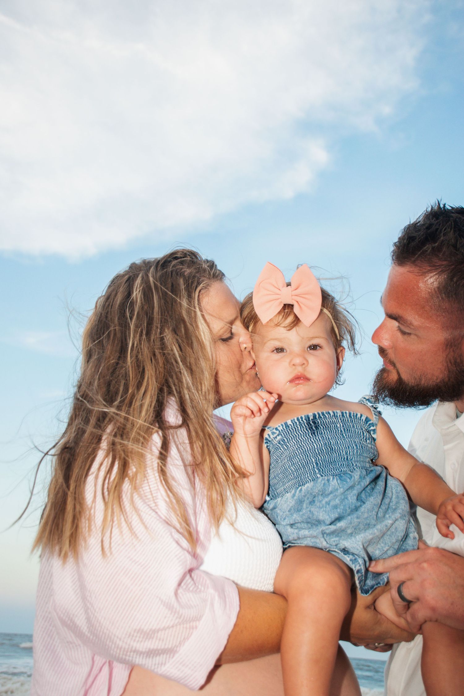 A family shares tender moments together at the beach with blue skies in the background.