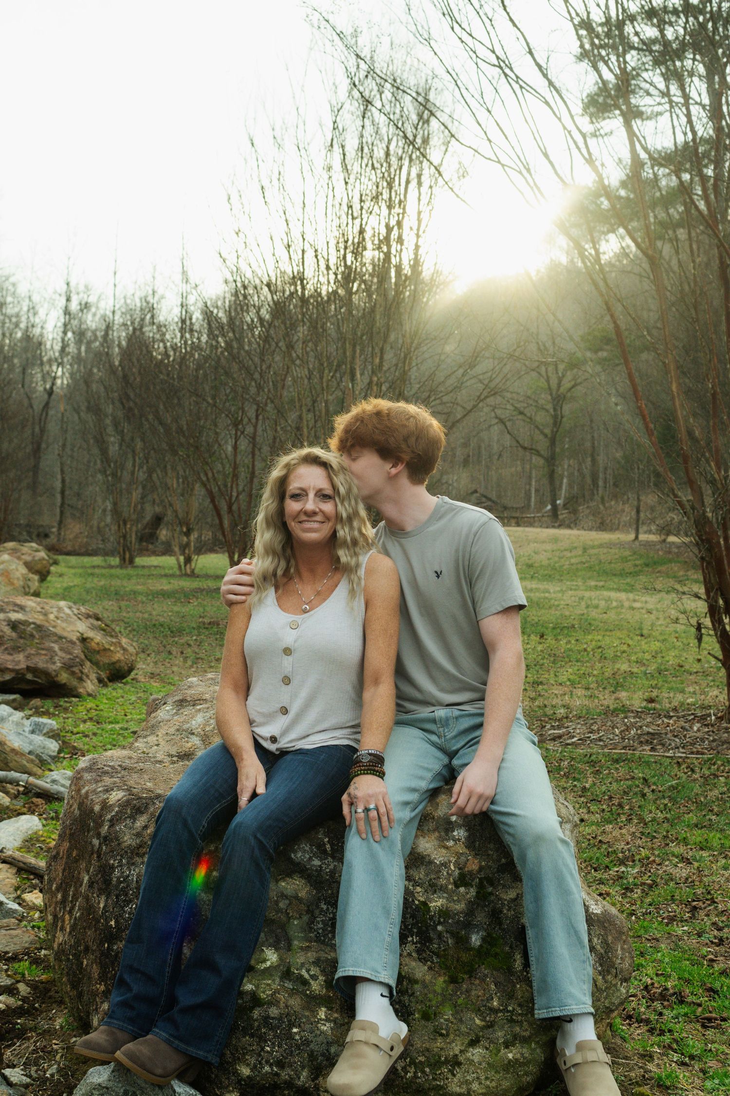 A couple sits together on a large rock in a natural outdoor setting during golden hour.