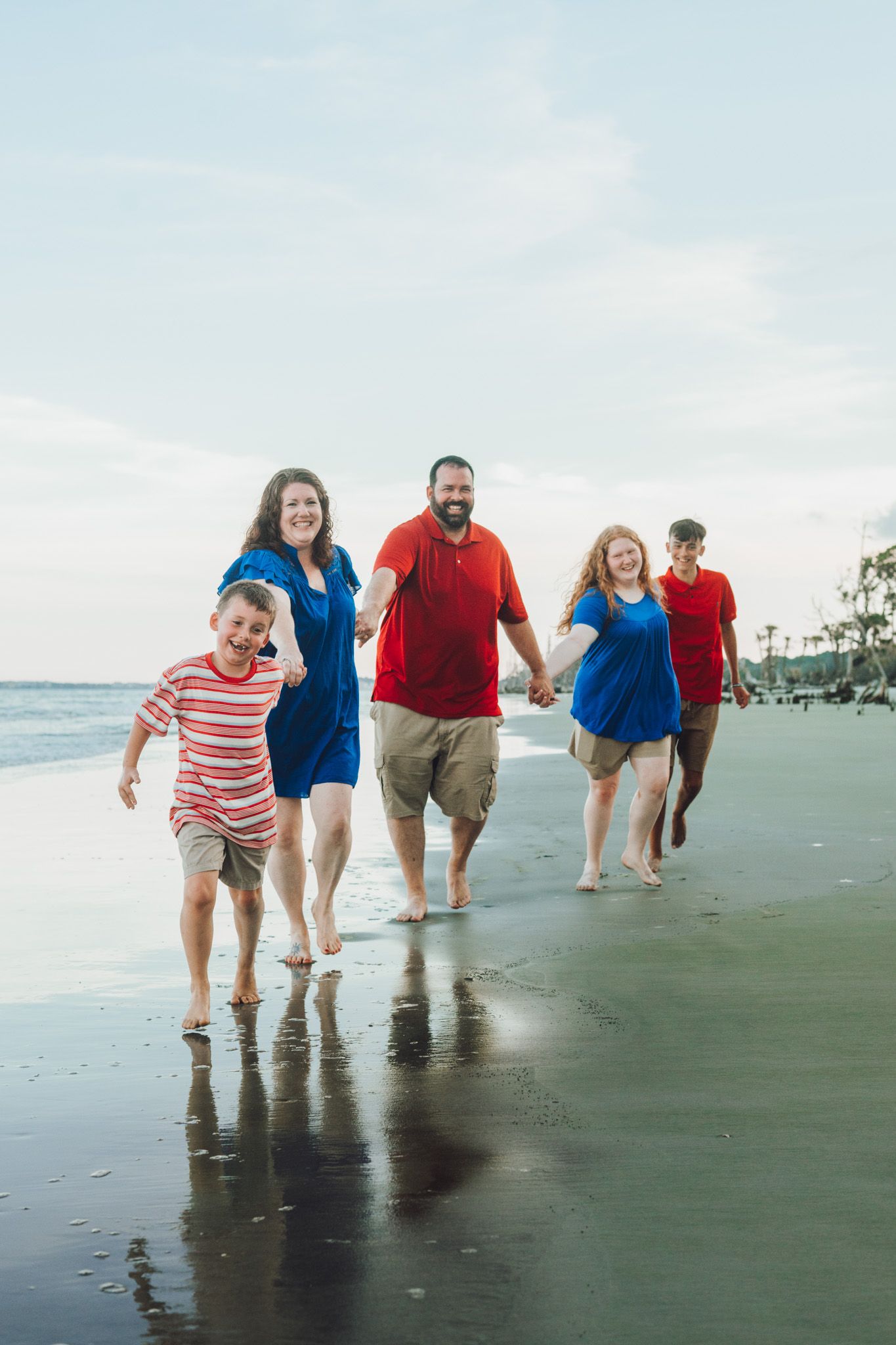Group walking together along a scenic beach shoreline at sunset with reflections in the wet sand.