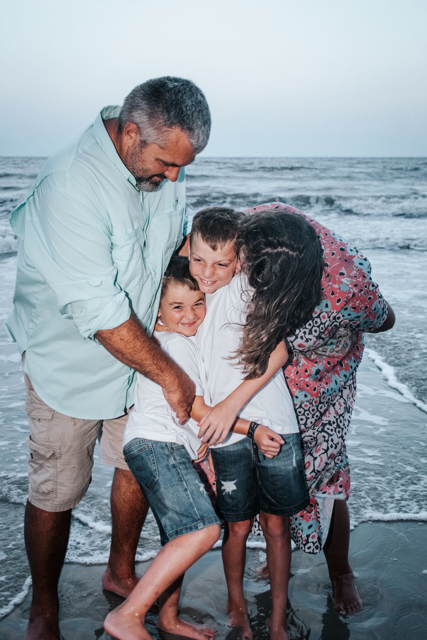 Family huddled together playing in ocean waves at dusk.