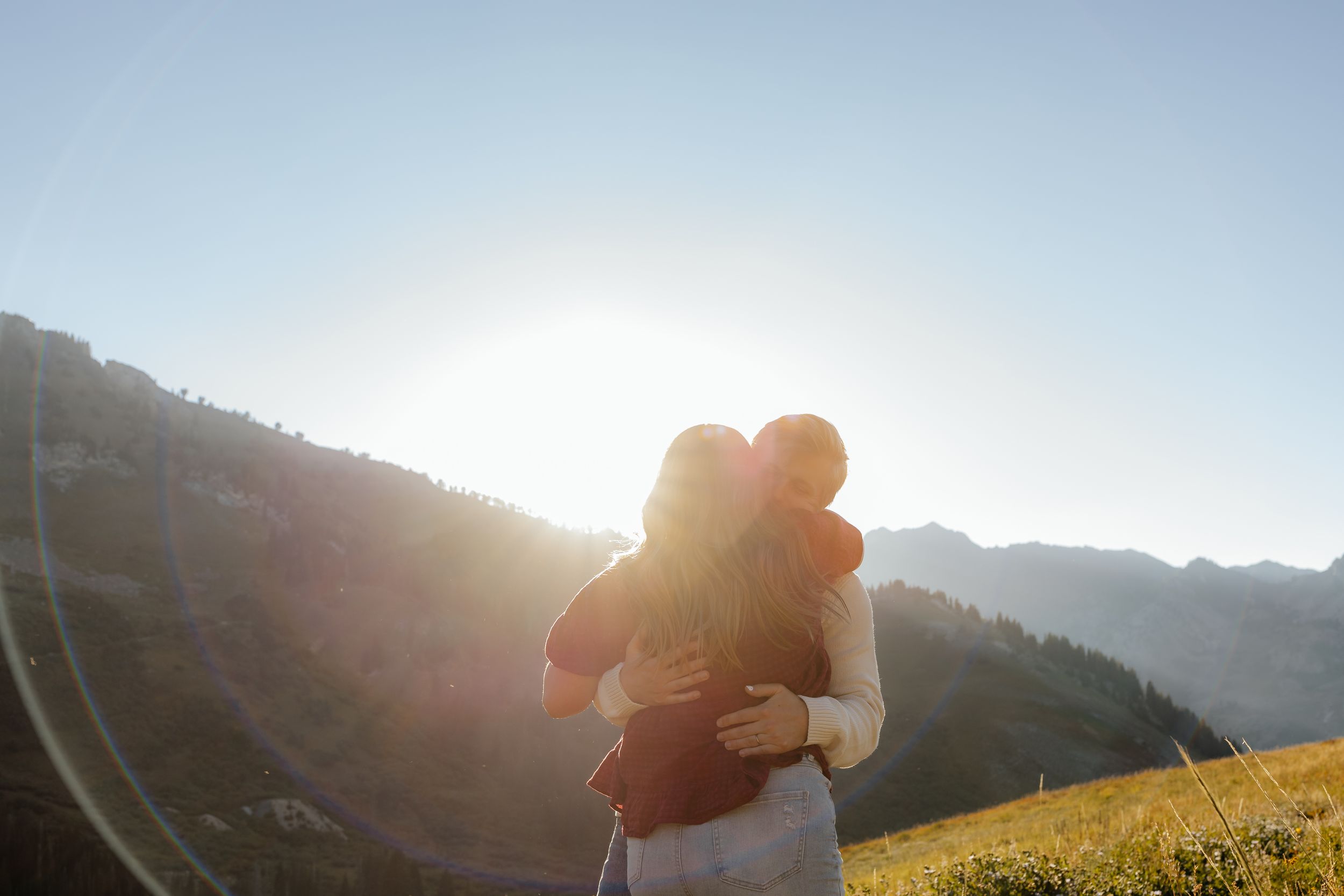 Couple embracing in golden sunlight with mountain landscape backdrop.
