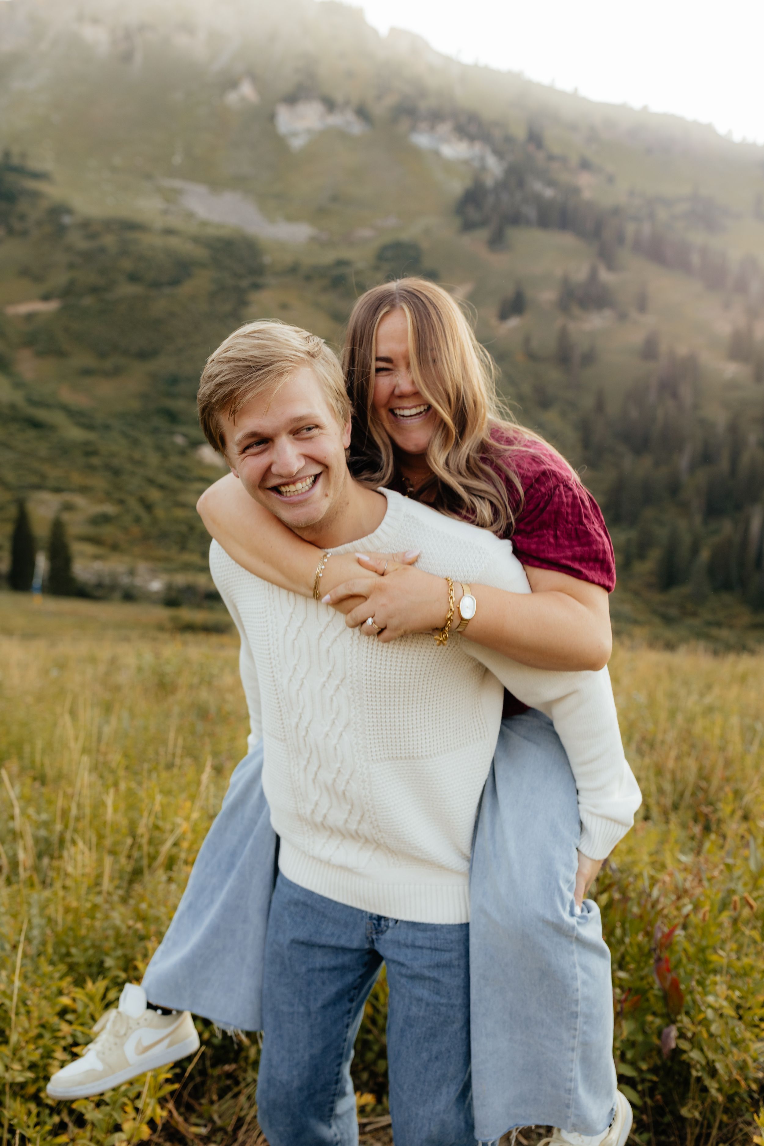 Smiling man giving woman a piggyback ride in alpine meadow.