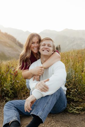 Happy couple sitting in mountain meadow, woman hugging man from behind.