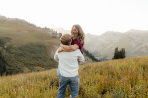Man lifting smiling woman in a golden mountain meadow at sunset.