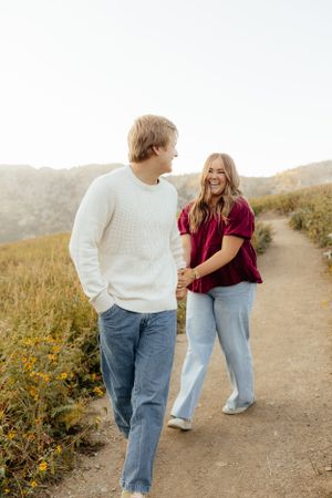 Laughing couple holding hands while walking on a mountain trail.