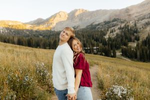 Couple holding hands back-to-back in a scenic alpine meadow.