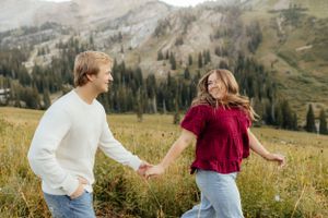 Joyful couple running hand-in-hand through a wildflower mountain meadow.