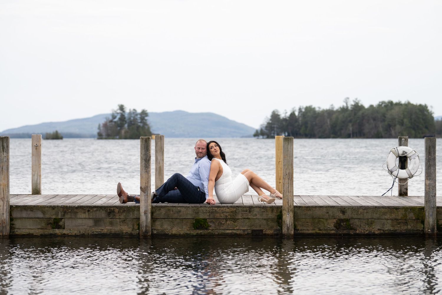 People relaxing on a wooden dock over a lake with mountains in the distance.