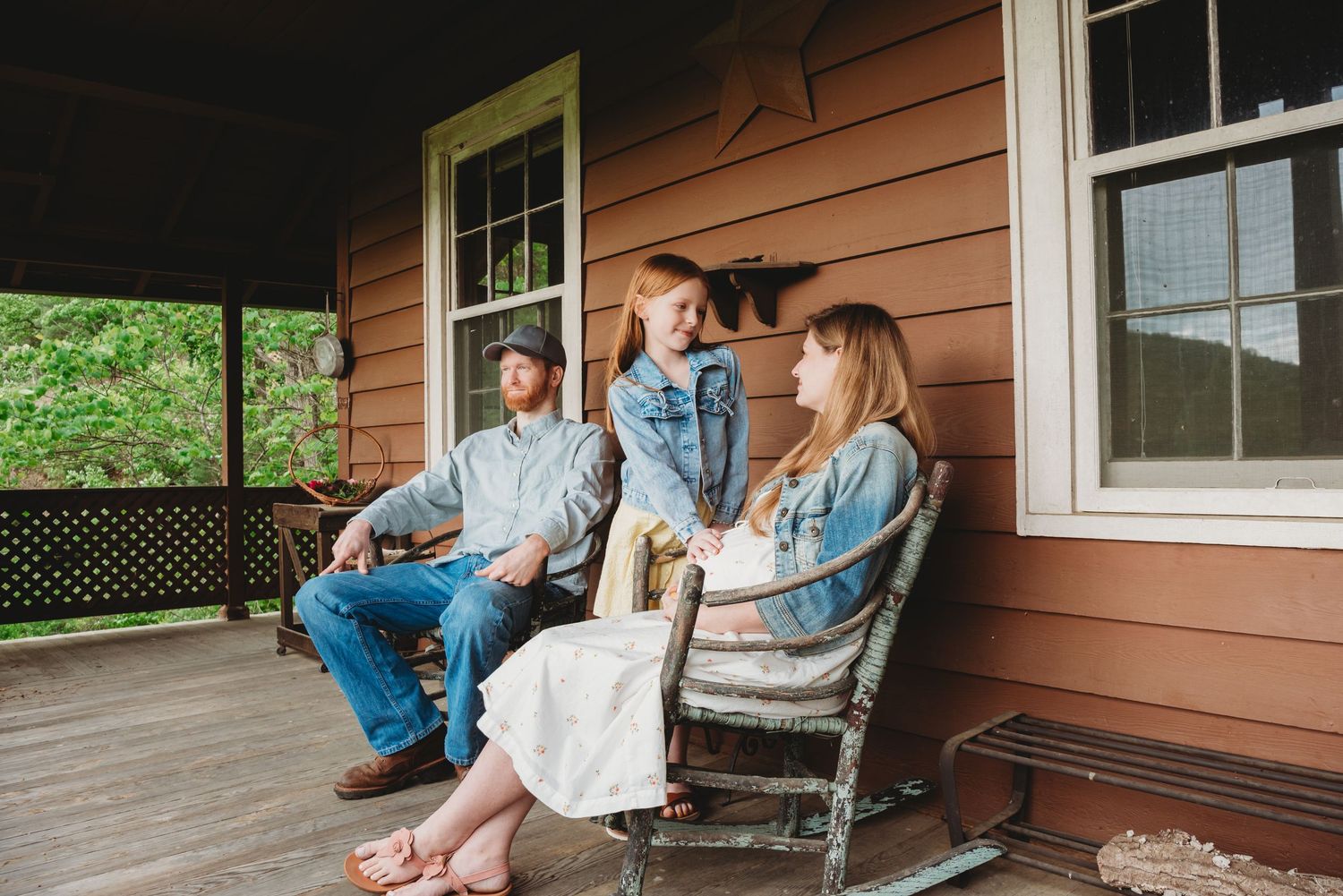 Family relaxing together on wooden rocking chairs on a rustic porch of an orange house.
