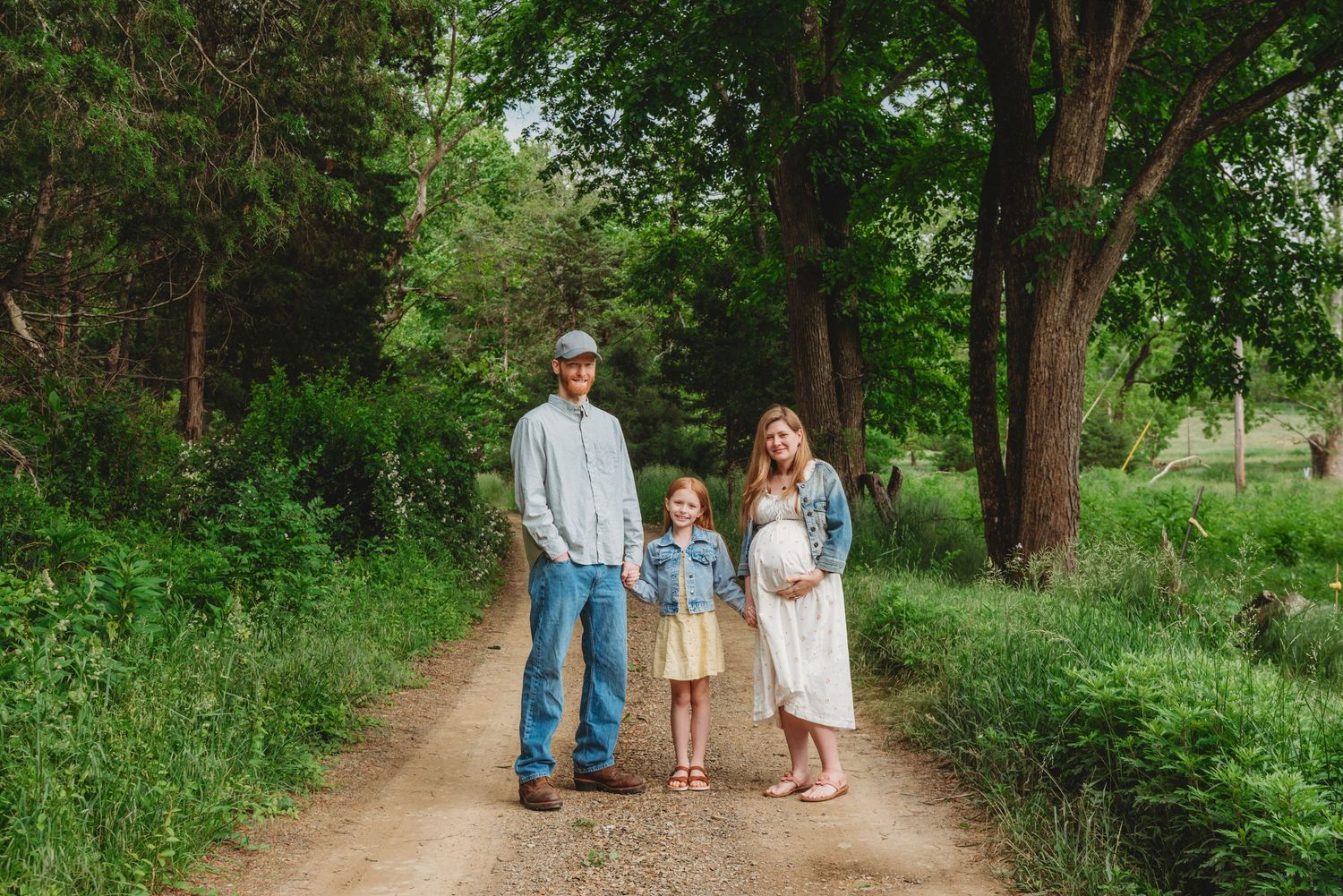 Family standing together on a dirt path surrounded by lush green trees.