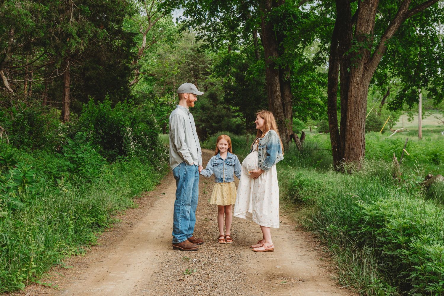 Family posing together on a tree-lined dirt path in natural setting.