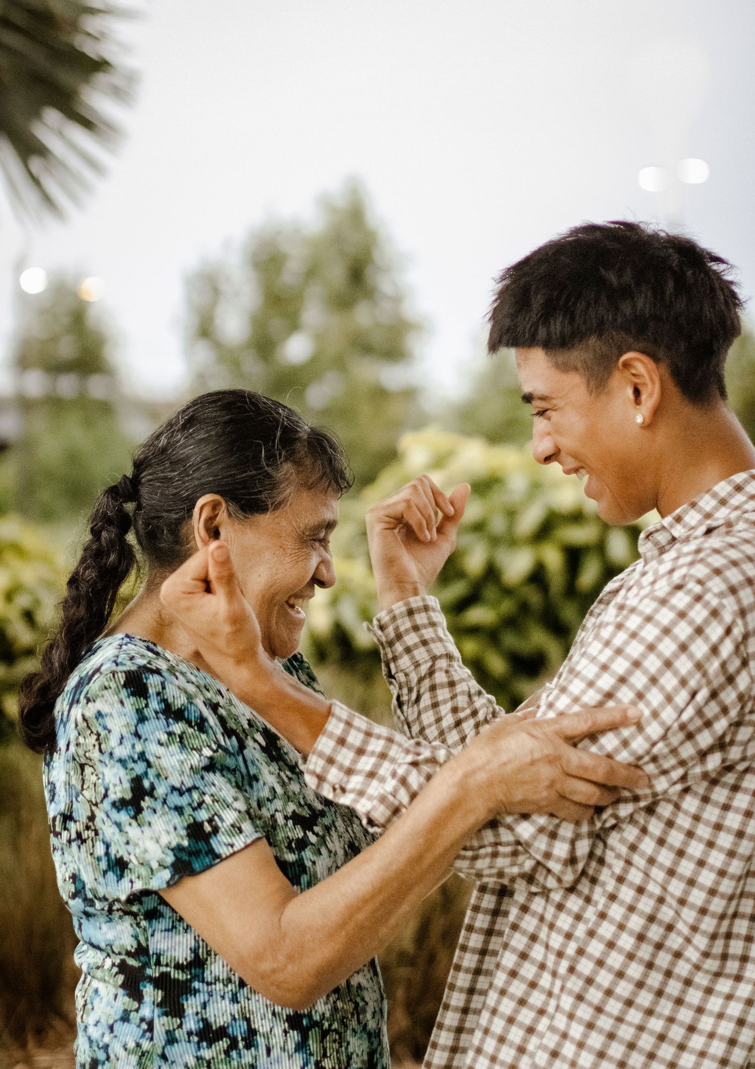 Elderly woman and young man laughing joyfully while dancing together outdoors in a garden.
