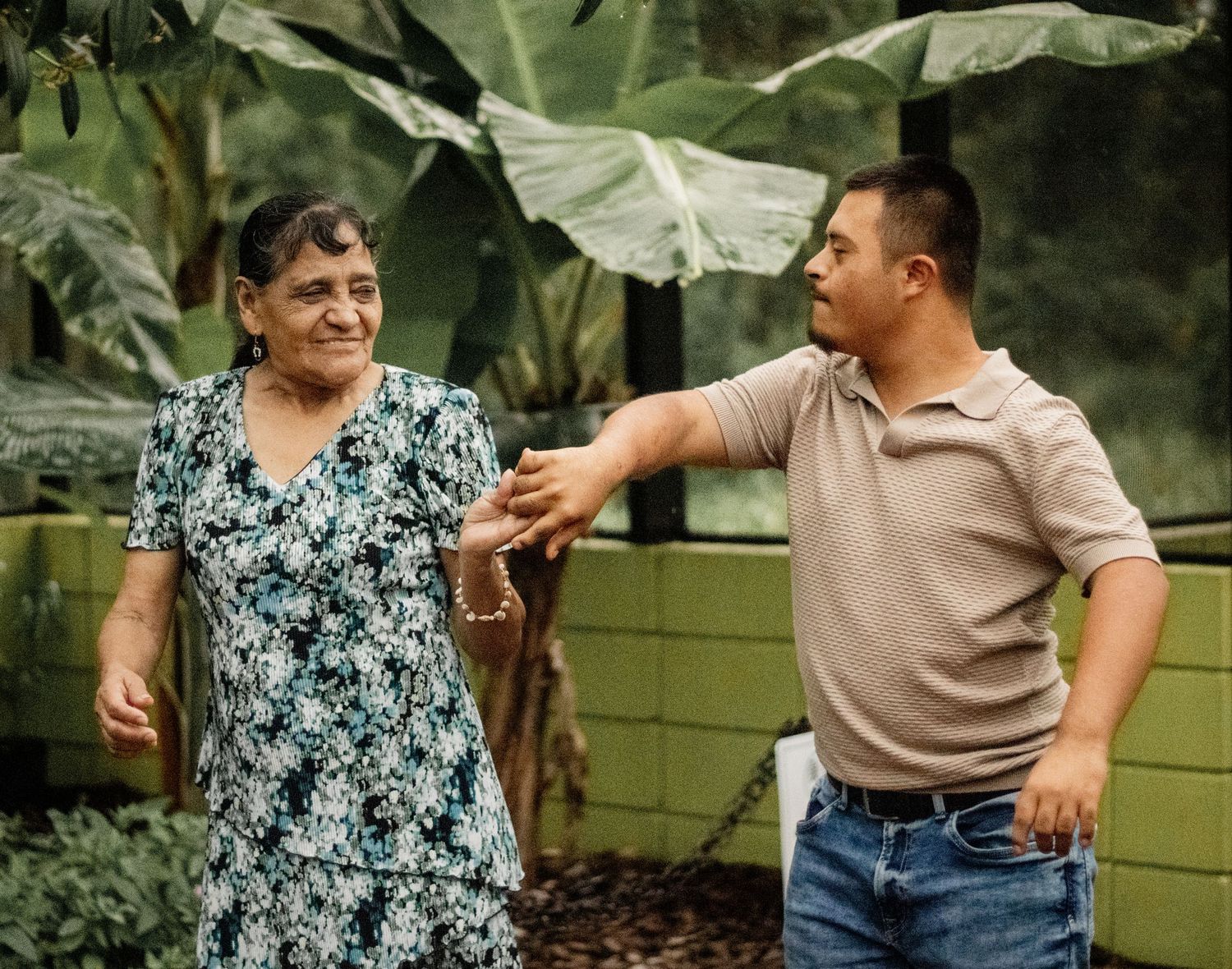 Elderly woman and young man sharing a warm moment together in a lush tropical garden setting.