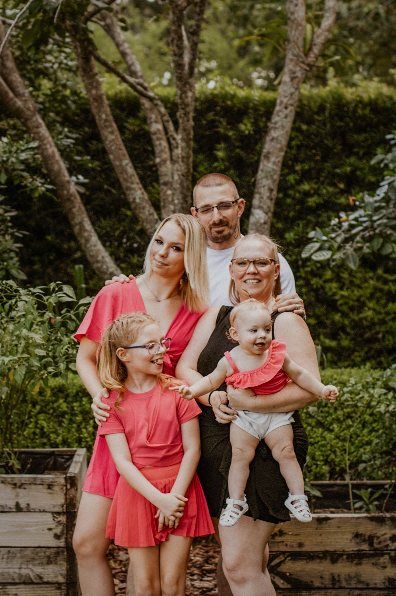 Family of five posing together in a wooded setting, wearing coordinated pink and white outfits.