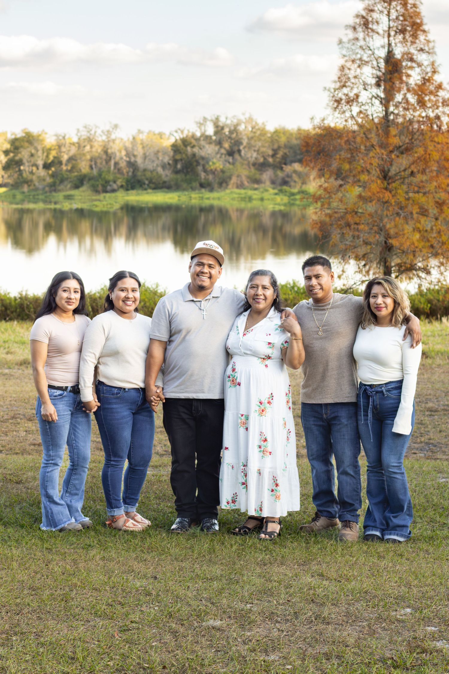 Family of six smiling together outdoors near a scenic lake surrounded by autumn foliage.