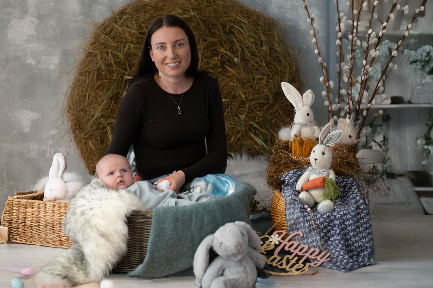 Easter themed portrait setup with baby lying on blue cushion surrounded by plush bunnies and spring decor.