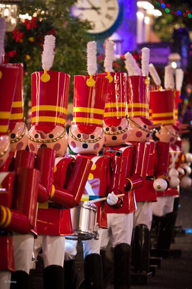 A row of toy nutcrackers in red and gold uniforms with white plumes displayed against a festive holiday background.