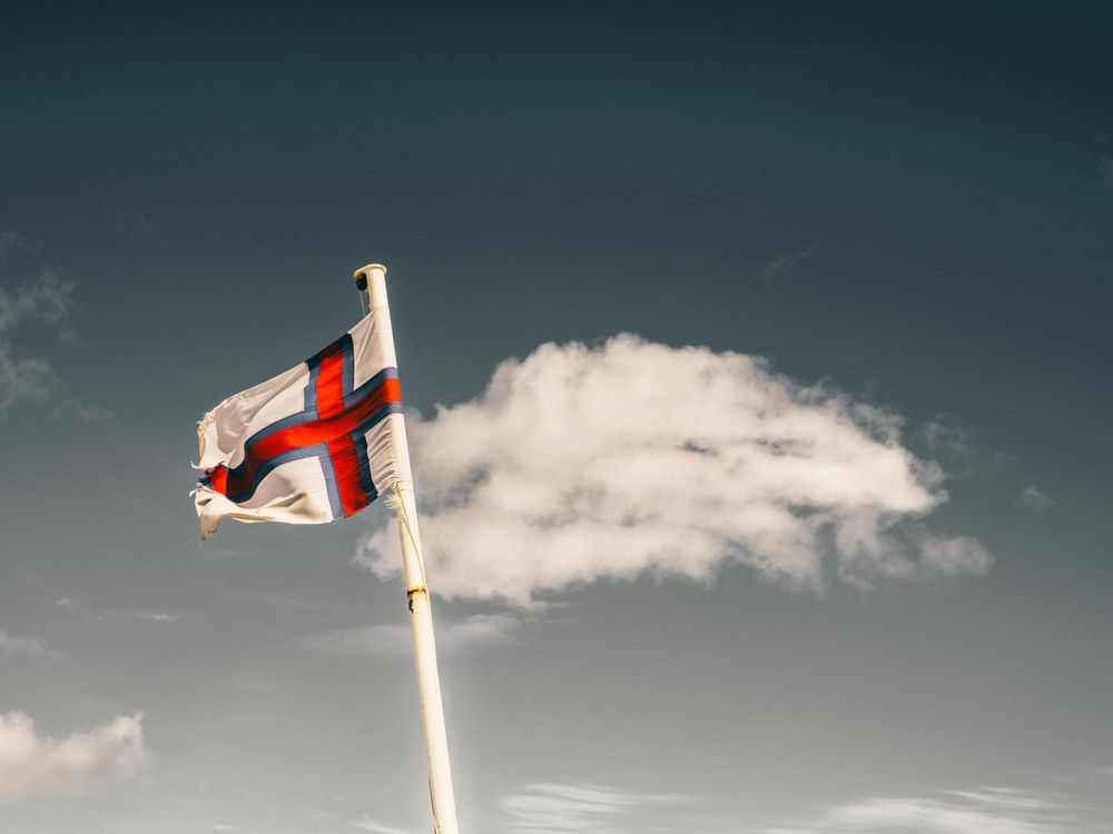 An English flag flies against a moody teal sky with a white puffy cloud in the background.