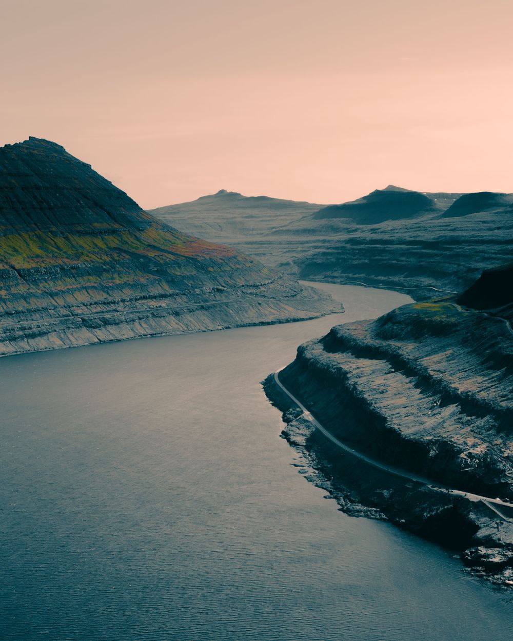 Panoramic aerial view of dramatic cliffs along a winding fjord coastline during twilight creating a moody atmosphere.