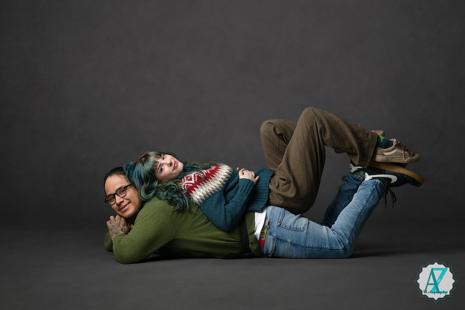 Two people in casual wear lying on their sides on a dark background studio floor.