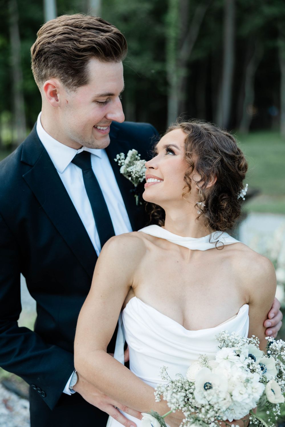 Happy bride and groom share a joyful moment outdoors with white flowers and natural scenery.