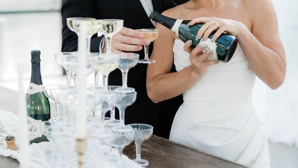 Champagne being poured into elegant coupe glasses at an elegant wedding reception.