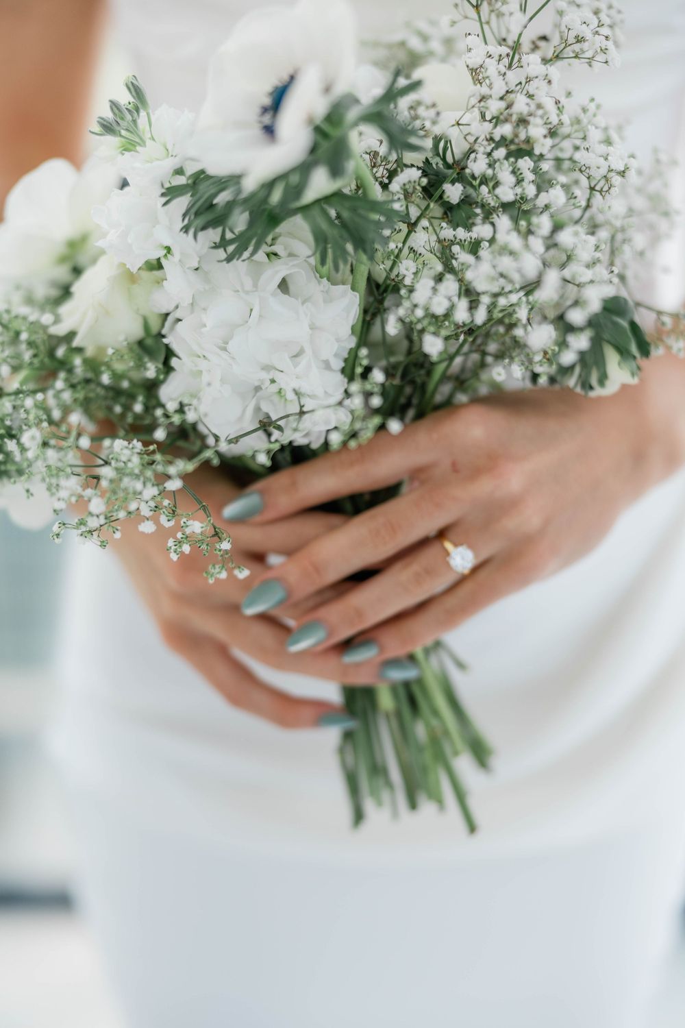 Close up of bride's hands holding delicate white and green wedding bouquet with baby's breath.