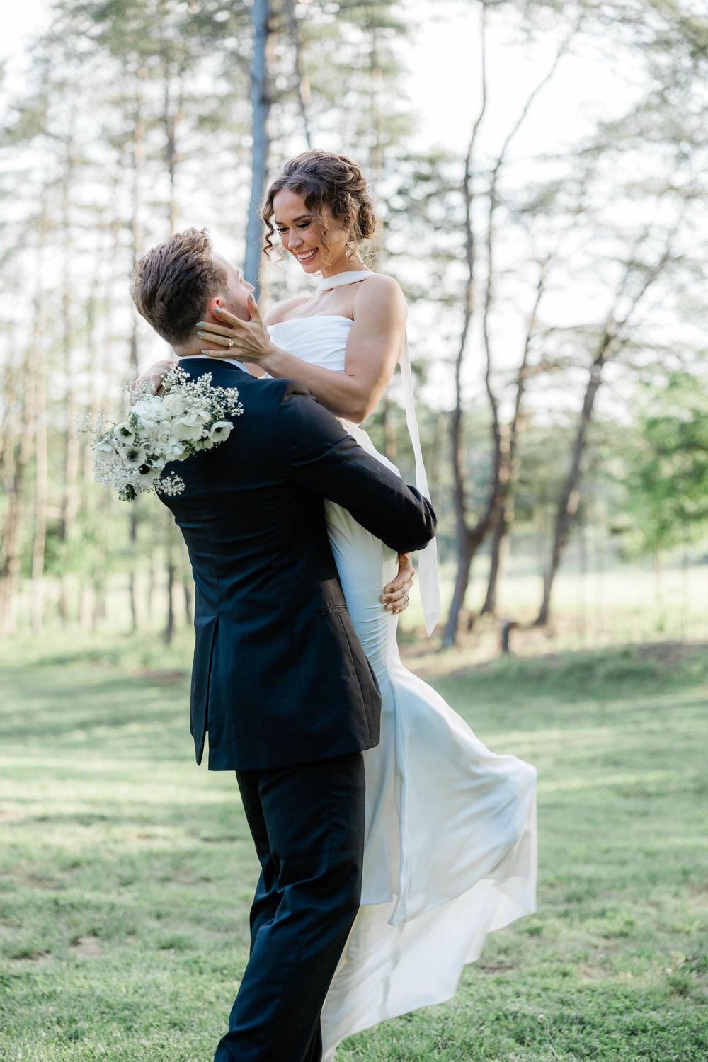 Joyful wedding couple dancing and embracing outdoors in a wooded setting.