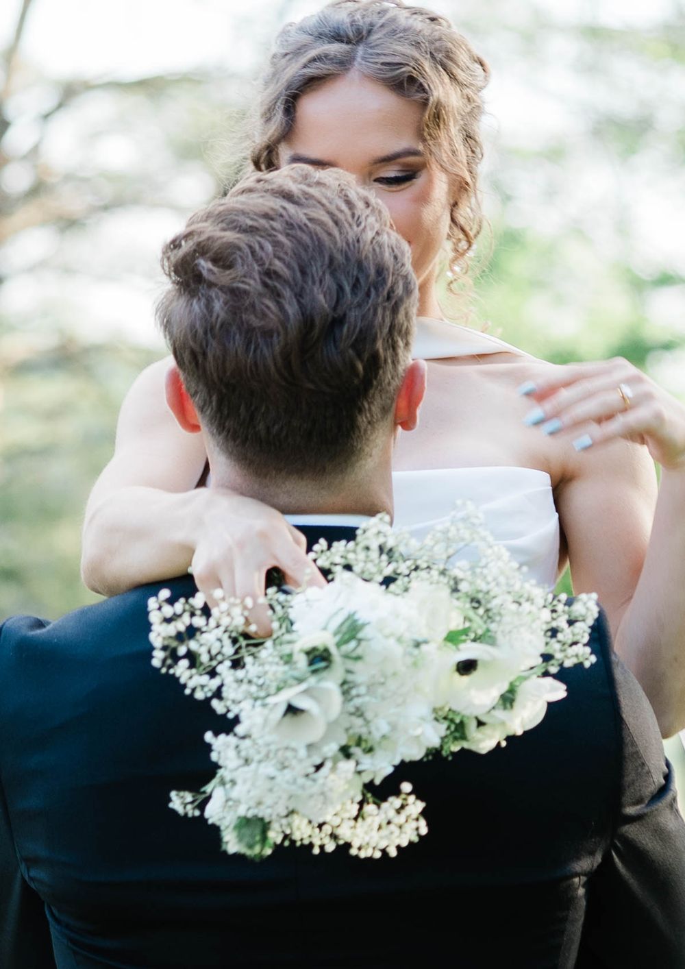 Intimate embrace between newlyweds with white floral bouquet outdoors.