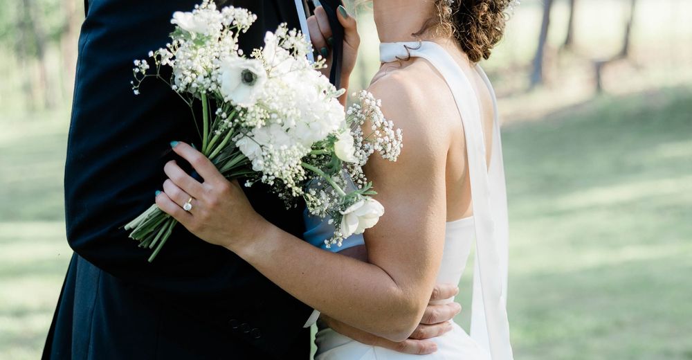 Romantic wedding couple holding white and blue floral bouquet in outdoor garden setting.