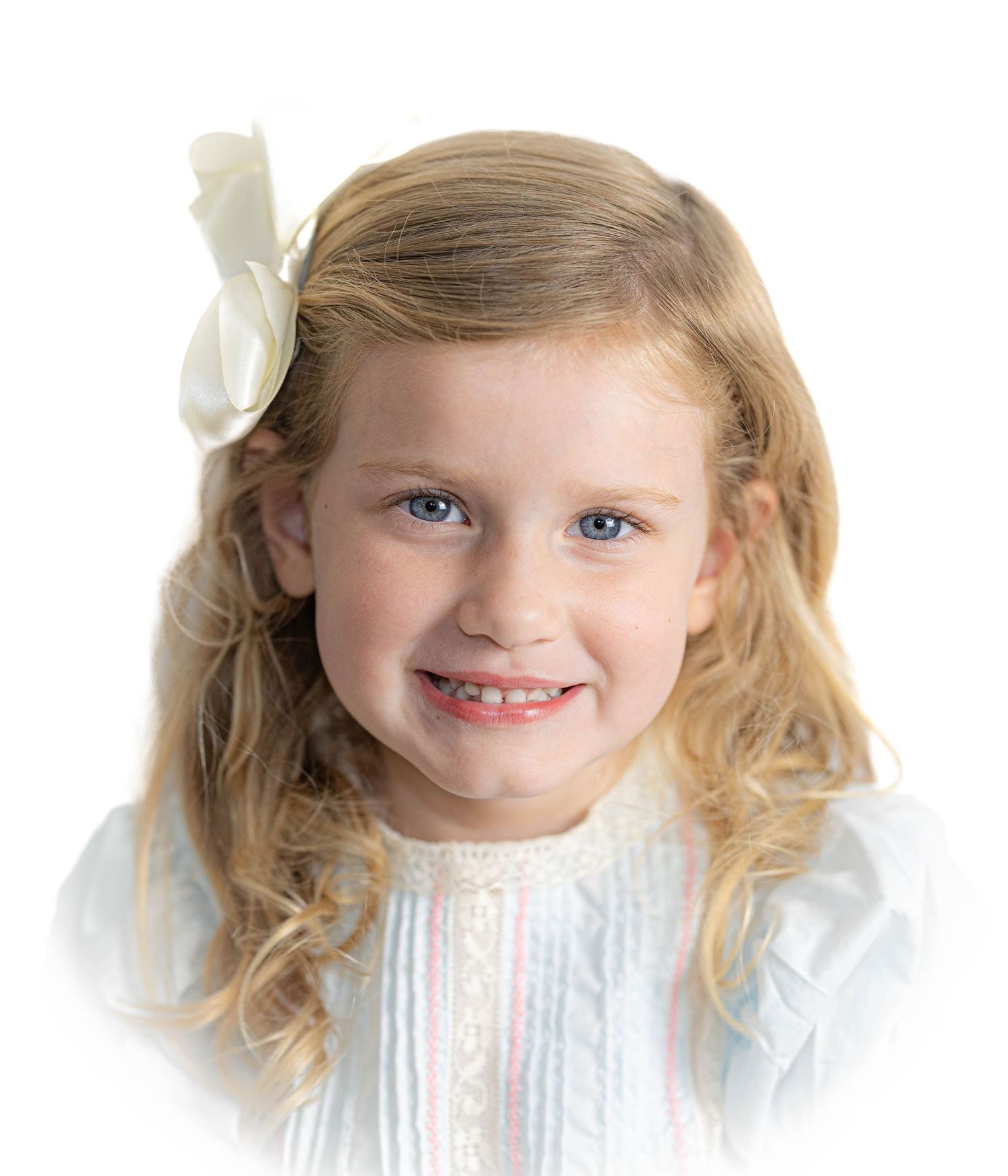 Young girl in white dress with bow hair accessory smiling at camera.