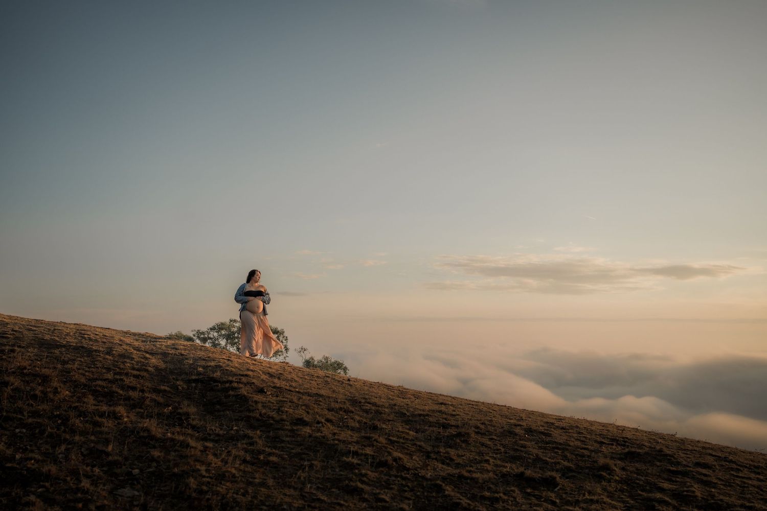 Silhouetted figure standing on misty hilltop during golden sunset.