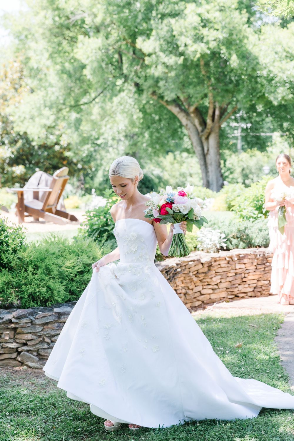 A bride in a classic white ball gown twirls joyfully in a garden setting while holding a vibrant floral bouquet.
