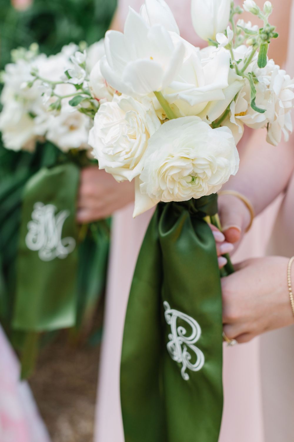White roses and flowers arranged on a light pink dress with monogrammed green sash showing an elegant wedding detail.