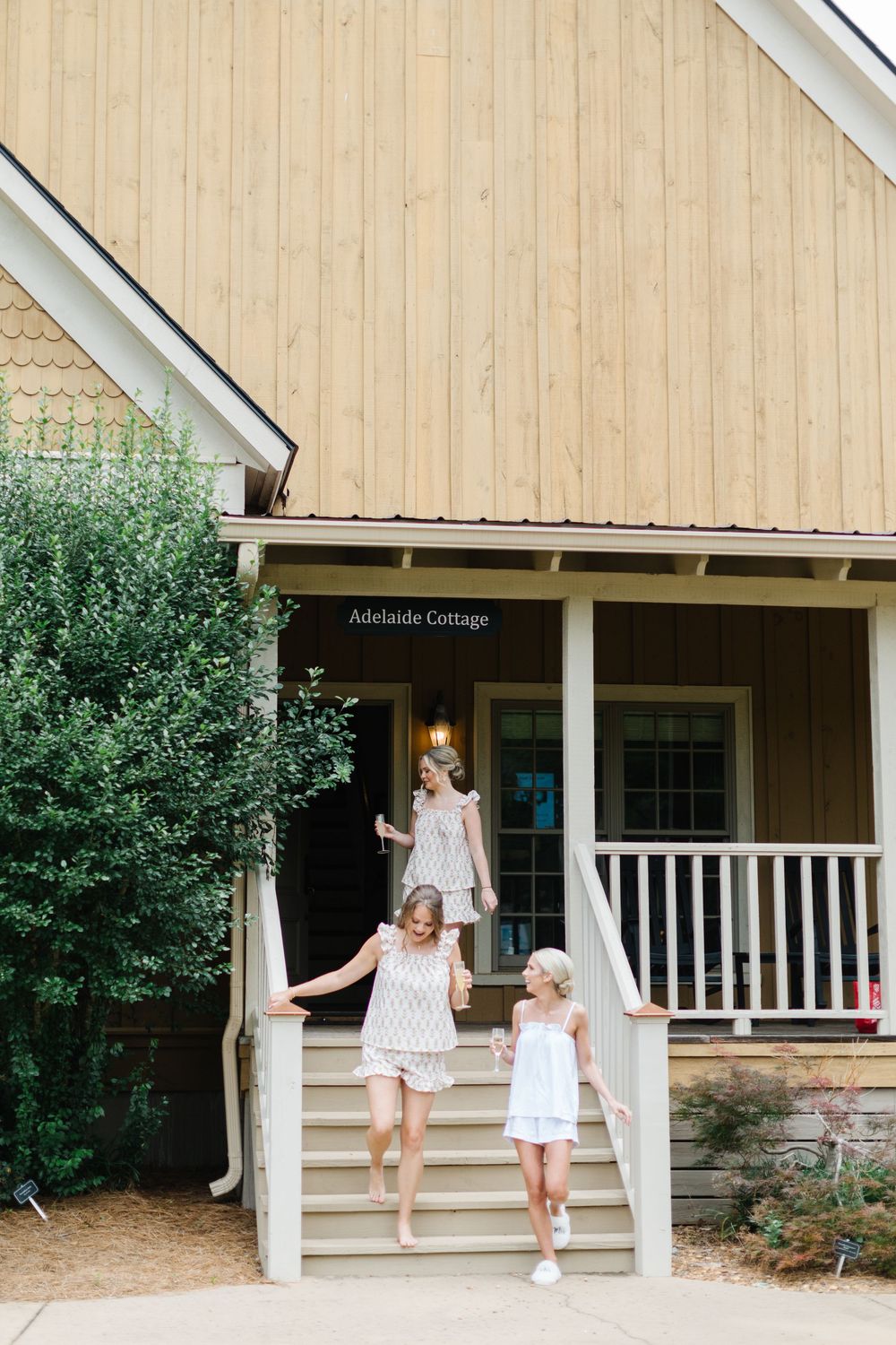 Three people in white dresses descending stairs outside Cottage entrance with wooden siding and porch.